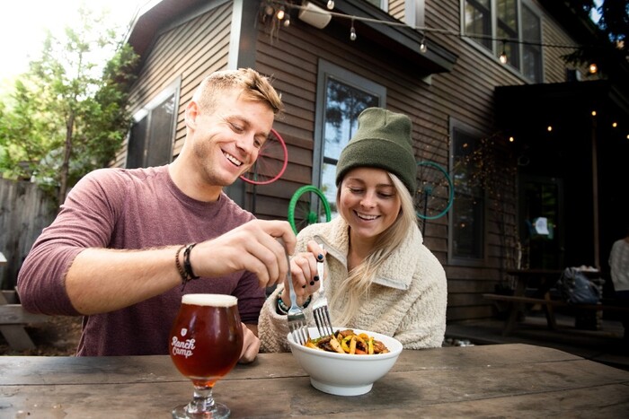 a couple sharing a bowl of food and a beer at an outdoor table at a restaurant